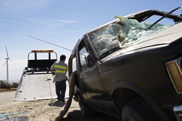 Rear view of a man preparing to lift crashed car onto tow truck