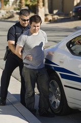Full length of a police officer arresting young man for breaking traffic rules