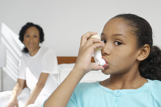 Portrait of a girl using asthma inhaler with mother in background