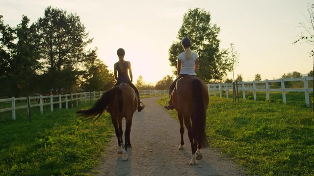 SLOW MOTION: Two girlfriends horseback riding brown horses into the sunset