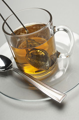 Closeup of a tea strainer dipped in cup filled with water over grey background