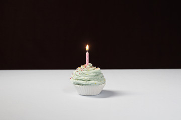 Baked cupcake with lighted birthday candle on table isolated over black background