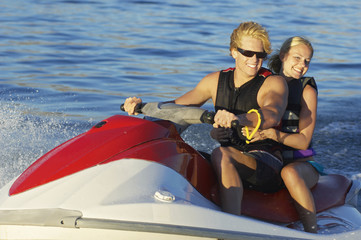 Happy young Caucasian couple riding personal watercraft on lake