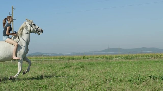 SLOW MOTION: Girl on beautiful white horse cantering bareback on grass field