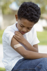 Closeup of an upset young boy looking at bandage on arm