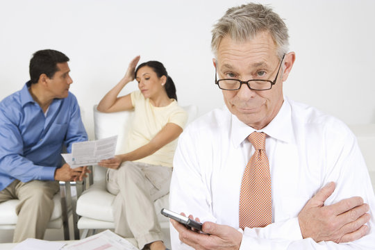 Senior Financial Advisor Holding Calculator With Couple Arguing In Background