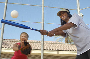 Two happy multiethnic female friends playing baseball