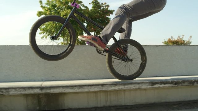 SLOW MOTION CLOSEUP: Extreme bmx biker jumping on bench and riding on back wheel