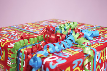Fototapeta na wymiar Closeup of a present wrapped with colourful paper and curly ribbon isolated on pink background