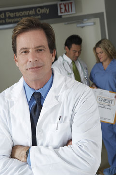 Portrait of male doctor in hospital with colleagues discussing in background
