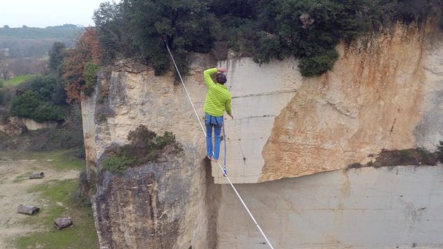 AERIAL: Active guy highlining with backup over quarry and trying to balance