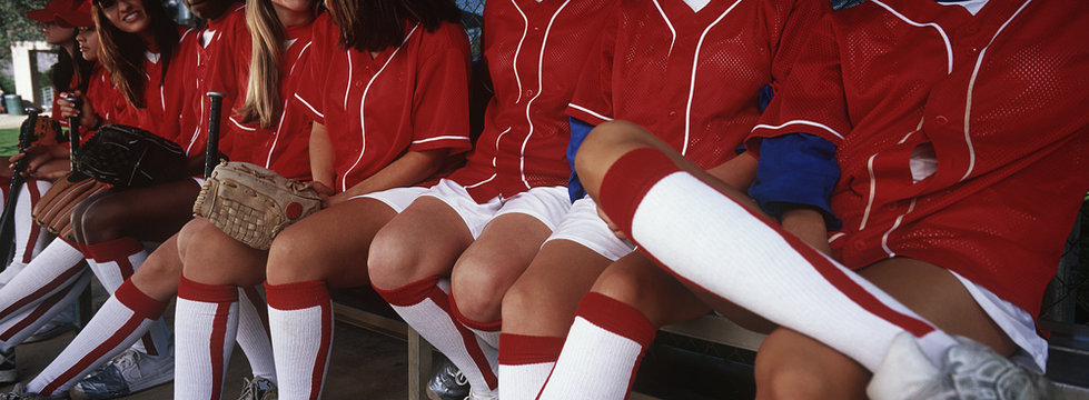Female baseball team players sitting together on bench