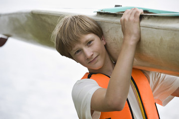 Closeup portrait of a teenage boy carrying kayak