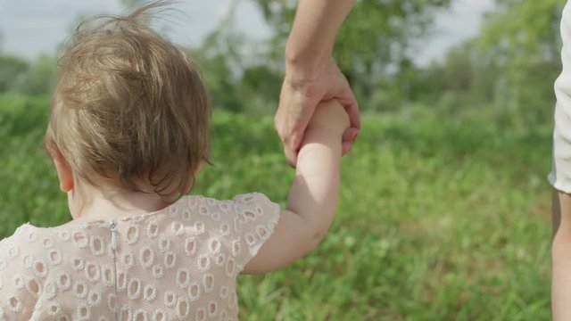 CLOSE UP, SLOW MOTION: Little Baby Girl Walking In Park, Holding Mother's Hand