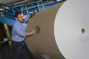 Man pushing huge roll of paper in newspaper factory