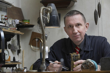 Portrait of confident middle aged repairman working on clock in workshop