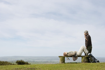 Obraz premium Full length side view of young woman relaxing on park bench with man looking at ocean