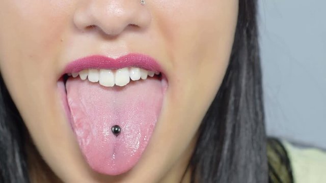 girl out her tongue at the camera: pierced tongue; woman with piercing