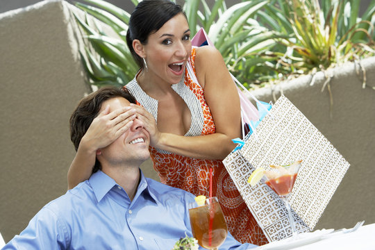 Portrait of a playful woman holding hands over man's eyes at cafe