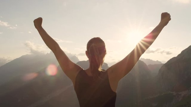 CLOSE UP: Young woman standing on the edge of the mountain with hands raised