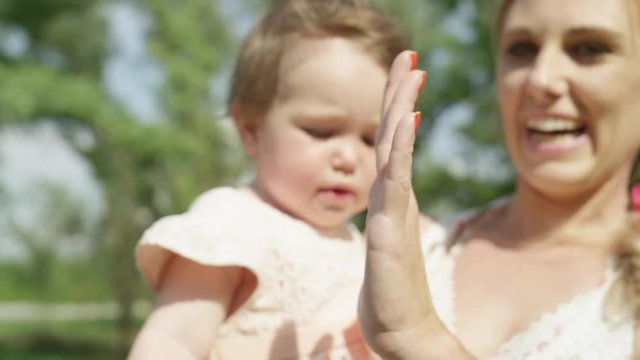 DOF, CLOSE UP: Pretty baby girl giving high five to her smiling beautiful mother