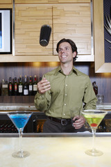 Handsome bartender tossing shaker in the air at bar counter