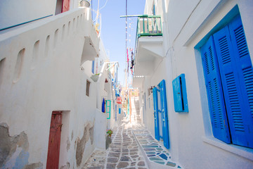 The narrow streets of greek island with blue balconies, stairs and flowers. Beautiful architecture building exterior with cycladic style.