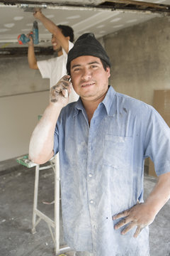 Portrait of Hispanic Latin construction worker on call with coworker working in background
