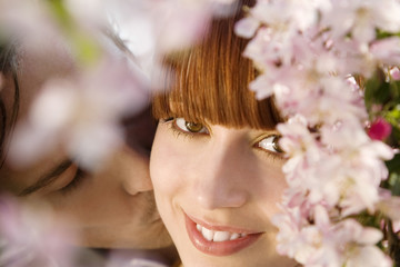 Fototapeta premium Closeup of young man kissing happy woman behind blooming cherry tree