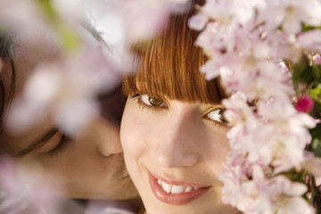 Closeup of young man kissing happy woman behind blooming cherry tree