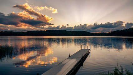 A dock jutts out into a lake at sunset on a northern Wisconsin lake. - Powered by Adobe