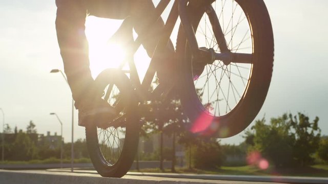 SLOW MOTION CLOSE UP: Bmx biker riding wheelie on back wheel on concrete bench