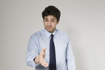 Portrait of young businessman offering hand to set a deal over grey background