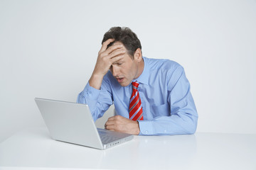 Businessman with hand on head looking at laptop isolated over white background