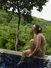 Fototapeta premium Side view of a bikini woman by swimming pool and against trees