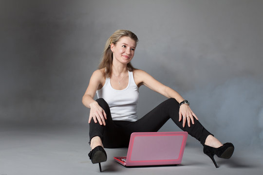 Young Beautiful Girl Is Dreaming With Pink Laptop Isolated On A Gray Background.