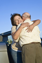 Happy senior couple standing in front of car and embracing