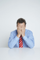 Depressed businessman covering face with hands at desk isolated over white background