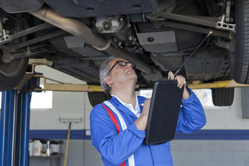Mechanic scrutinizing the car and writing down something on clipboard