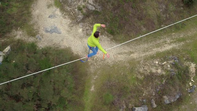 AERIAL: Courageous slackliner sitting on highline over abyss and standing up