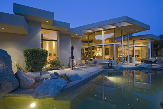 Illuminated House Exterior With Swimming Pool In Backyard At Dusk