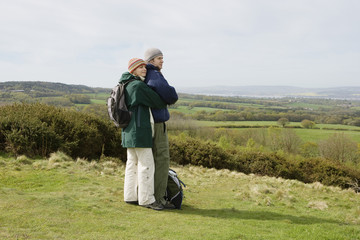 Full length of romantic young couple with backpacks embracing in field