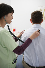 Doctor examining male patient's back using stethoscope in the clinic