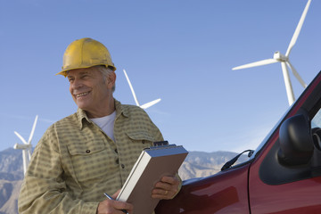 Smiling senior male wearing hardhat at wind farm