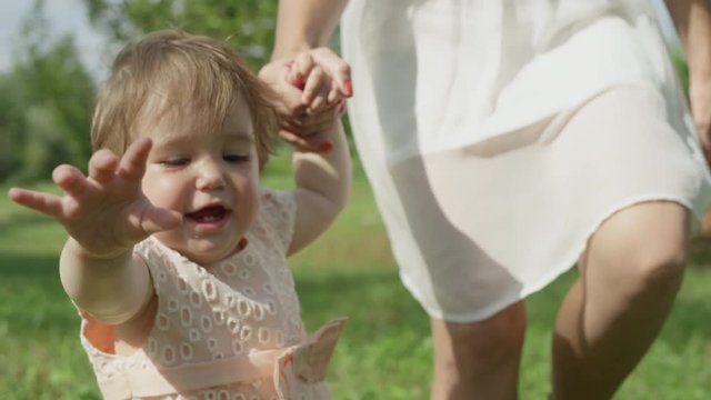 CLOSE UP SLOW MOTION: Happy baby girl walking in park, holding hands with mother