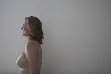 Side view of a smiling blond woman in bra against gray background