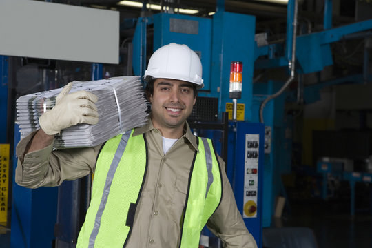 Portrait of a smiling industrial operator carrying newspapers in factory