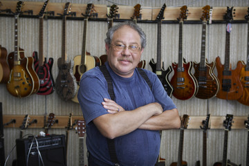 Portrait of middle aged male music store owner standing arms crossed