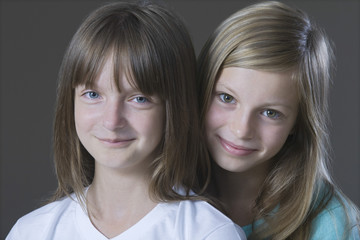 Closeup portrait of two young girls smiling against gray background