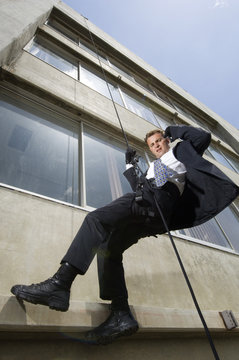 Low Angle View Of A Spy Rappelling While Using Mobile Phone